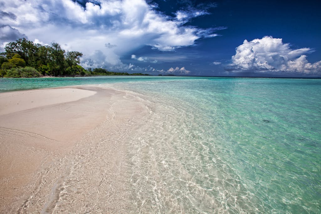 Idyllic tropical beach with clear turquoise water and lush greenery under a vibrant sky.